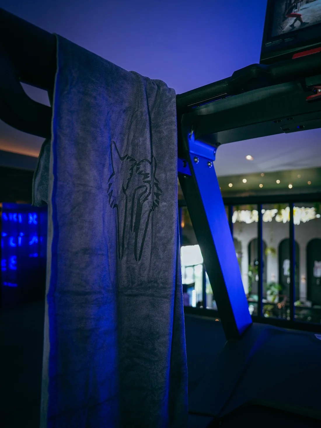Savage Elite Fitness wolf towel draped over equipment on the training floor under ambient blue gym lighting.